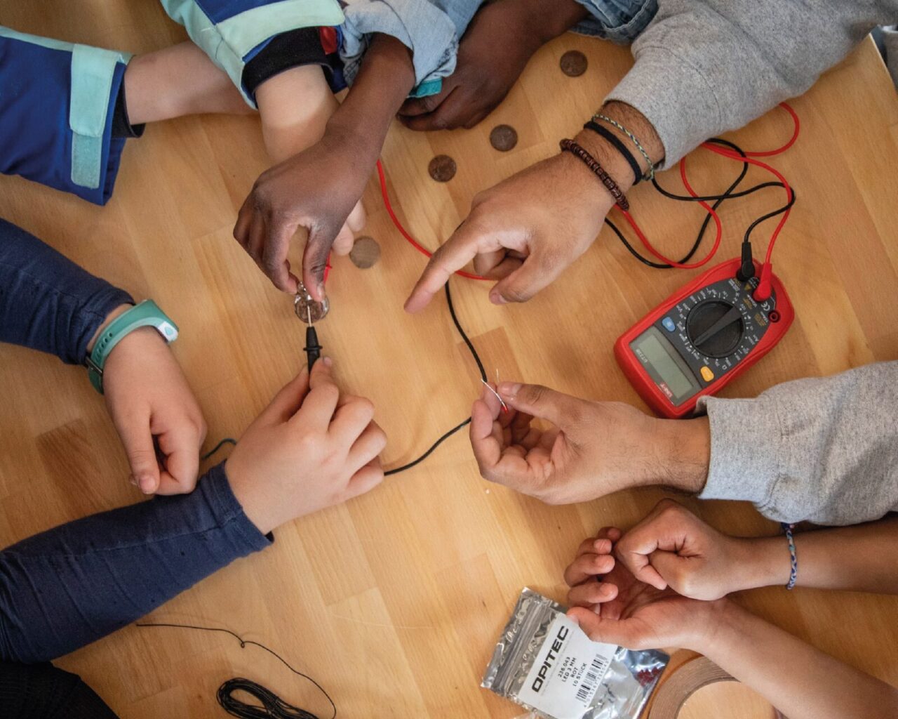 Photographie prise de l'atelier Carte lumineuse, gros plan sur les mains des jeunes participants qui testent la conductivité